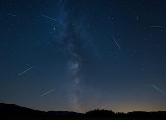Astronomski događaji 2025, Noćno nebo sa kišom meteora tokom Perzeida iznad mirnog pejzaža, uz vidljivu Mliječnu stazu i siluete drveća.