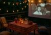 Ljetno kino na balkonu s lampicama, bokalom s voćem, jastučićima i projekcijom filma u toploj večeri