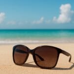 naočale za sunce, Sunčane naočale na pješčanoj plaži s pogledom na more i plavo nebo/ INZ